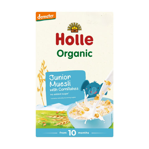 A box of Demeter Holle Organic Junior Muesli with Cornflakes, designed for children from 10 months. The packaging features a cream-colored background with red and green text, a blue elephant character, and an illustration of a bowl of cereal with milk splashes.